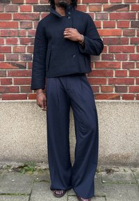 Granatowa krótka kurtka z wysokim kołnierzem i dwoma guzikami, zestawiona z szerokimi granatowymi spodniami, prezentująca gładką fakturę tkaniny.
