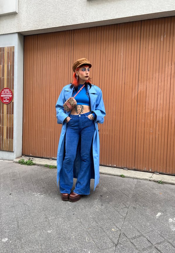 Casaco longo azul claro sobre um top cropped azul, combinado com calças de ganga azuis largas e sapatos de plataforma castanhos. Uma carteira estampada estava pendurada.