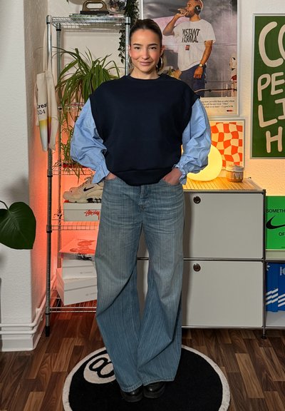 Sudadera oversize azul marino con mangas globo en azul claro, combinada con vaqueros de pierna ancha en azul claro y botas negras con plataforma, en un entorno moderno.