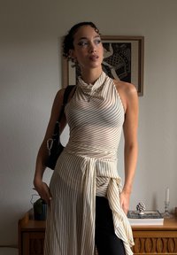 Top halter alb și bej cu dungi, cu guler plisat și imprimeu asimetric. Asortat cu pantaloni negri și o geantă mică neagră.