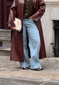 Bordeaux leren trenchcoat, bruine gebreide trui, lichtblauwe wijde spijkerbroek, metallic sneakers, met een crèmekleurige clutch. Textuur en oversized silhouet.