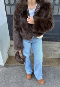 Hnedá krátka bunda z umelého kožušiny s kapucňou, svetlomodré džínsy a hnedá pletená kabelka. Celý vzhľad dopĺňajú hnedé platformové topánky.