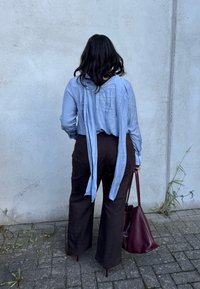 Blusa azul clara com laços nas costas, mangas longas e pregas; combinada com calças largas castanhas escuras e uma bolsa texturizada burgundy.
