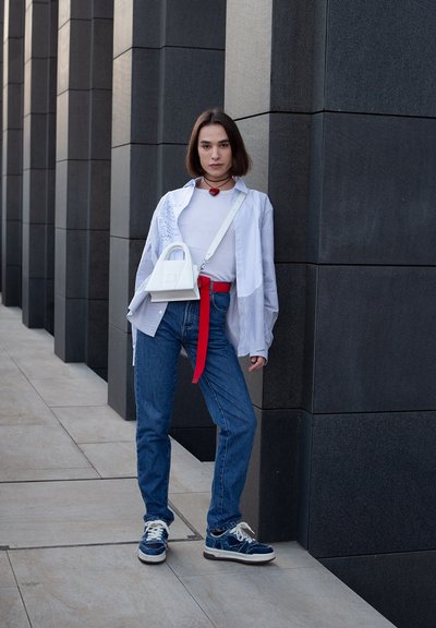 Modelo con una camiseta blanca, camisa de rayas oversized, cinturón rojo y jeans azules. Los accesorios incluyen un bolso blanco y zapatillas con detalles en azul oscuro.
