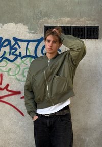 Alyvuogių žalumos trumpa bombonešio striukė su užtrauktuku priekyje ir ribinėmis rankogaliais. Dėvima ant baltos marškinėlių, derinama su juodomis džinsinėmis kelnėmis.