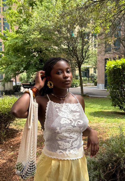 Top de tirantes blanco de ganchillo con patrón floral, combinado con una falda amarilla clara. Los accesorios incluyen pendientes de aro dorados y una bolsa de red.