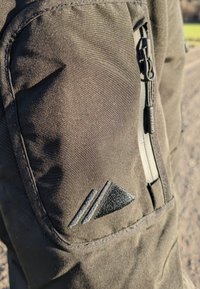 Črne zunanje hlače z stranskim žepom na zadrgo, ki imajo teksturirano blago in vezeno trikotno logo na stegnu.