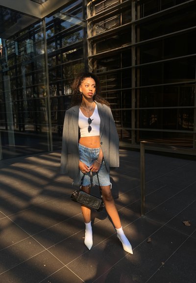 Un blazer gris de gran tamaño, una camiseta sin mangas blanca y corta, unos pantalones cortos de mezclilla desgastados, calcetines tobilleros blancos y tacones blancos puntiagudos; bolso negro.