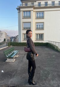 Sac à main bordeaux au design structuré avec ferrures argentées ; pull en maille texturée ; mini-jupe en cuir noire ; collants noirs opaques ; bottes noires montant jusqu'aux genoux.