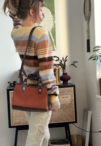 Sac à main en toile marron avec des accents en cuir foncé et des ferrures en métal. Pull rayé aux couleurs atténuées. Pantalon cargo de couleur claire.