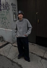 Striped grey and black jumper with ribbed texture and round neckline, paired with dark wide-leg jeans and black shoes. Beanie with logo detail.
