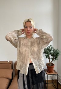 Beige, průhledná košile na knoflíky s pomačkanou strukturou a nabíranými rukávy. Obsahuje klasický límec a jemné stříbrné knoflíky.