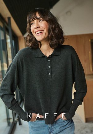 Dunkelgrünes, langärmeliges Poloshirt mit Kragen und drei Knöpfen vorne, aus weichem Stoff, kombiniert mit hellblauen Jeans.