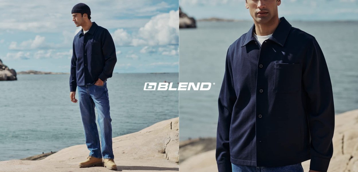 Marineblaues Hemdjackett mit einer Fronttasche, Knopfverschluss und spitzem Kragen, kombiniert mit hellblauen Jeans und beigem Schuhwerk.