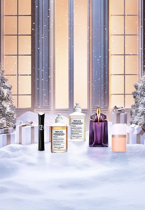 Five perfume bottles displayed on snowy surface: black tube, gold and white bottles labeled "REPLICA," purple bottle, pink bottle with metallic cap.