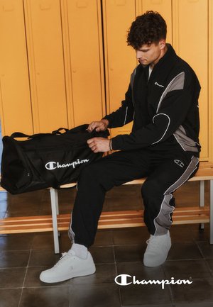 Completo sportivo nero e grigio, con strisce a contrasto, giacca con zip e pantaloni con vita elastica. Borsa a tracolla nera con logo.