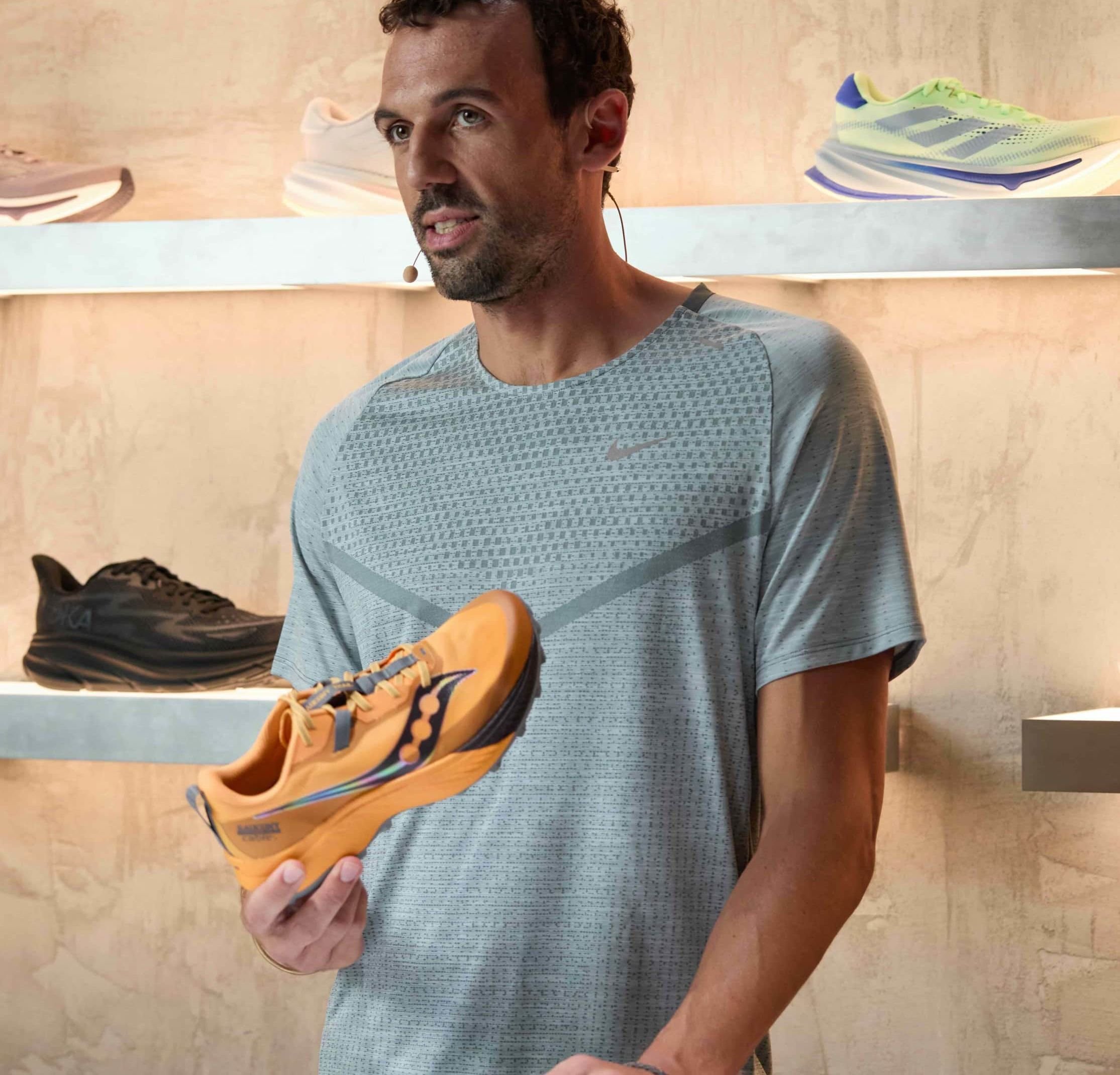 Orangene Laufschuhe mit schwarzen Akzenten, strukturiertem Obermaterial und Schnürverschluss; leichtes Design, präsentiert von einer Person in einem grauen Shirt.