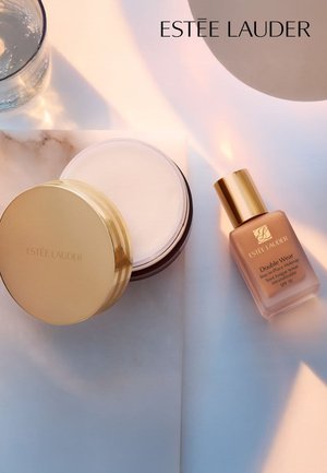 Estee Lauder Double Wear foundationfles in beige, met gouden accenten, naast een ronde crèmejar met gouden deksel op een lichte ondergrond.