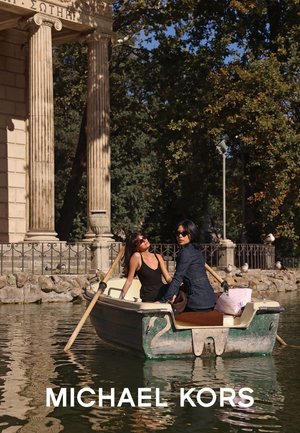 Deux individus dans un petit bateau sur un étang. Le bateau est vert avec des accents en bois. L'arrière-plan comprend une architecture classique et des arbres.