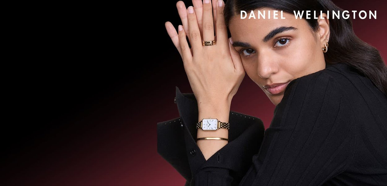 Zegarek w złotym kolorze z kwadratową, białą tarczą i metalową bransoletą. Czarna koszula na guziki z pionowymi paskami. Prosty złoty pierścionek i bransoletka jako dodatki.