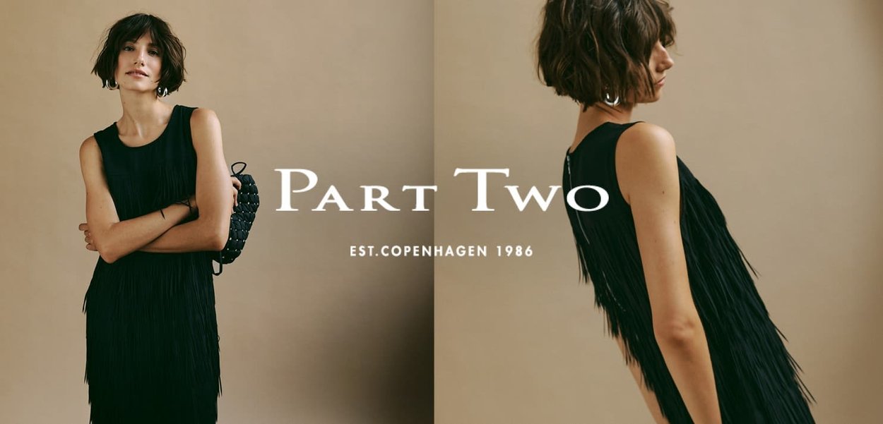 Abito nero senza maniche con dettagli di frange. Modella in posa con le braccia incrociate, indossando una borsa a tracolla nera intrecciata. Sfondo neutro.