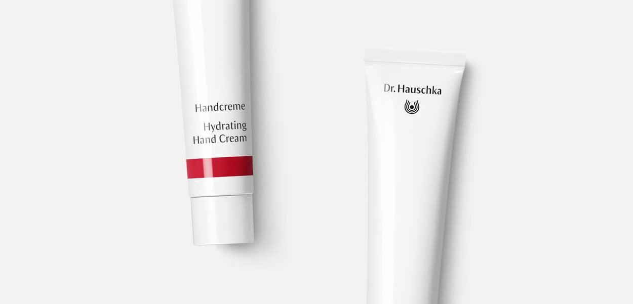 Zwei weiße Tuben Handcreme, eine mit der Aufschrift "Hydrating Hand Cream" und einem roten Akzent, die andere mit "Dr. Hauschka" und einem schlichten Logo.