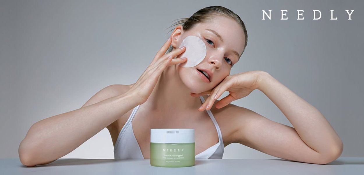 NEEDLY Euctact Oblitang pod; round green container with white lid, model applying a circular pad to her face, smooth skin, minimalistic background.