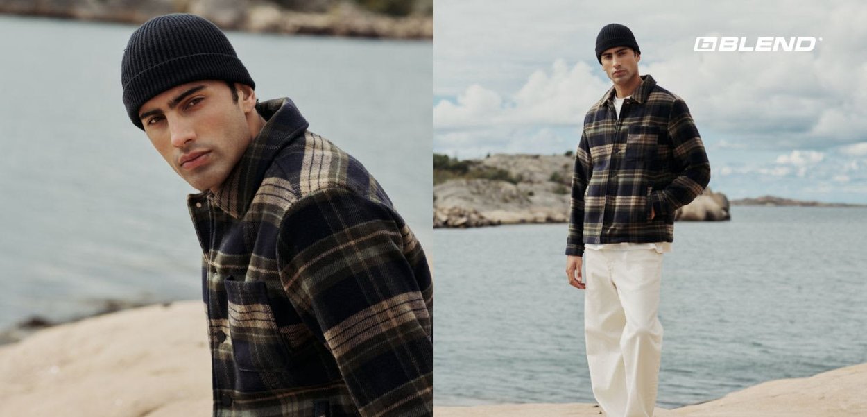 Giacca in pile a quadri nei toni del blu scuro, crema e beige, con collo a camicia e taschino sul petto. Abbinata a pantaloni bianchi e un berretto nero.