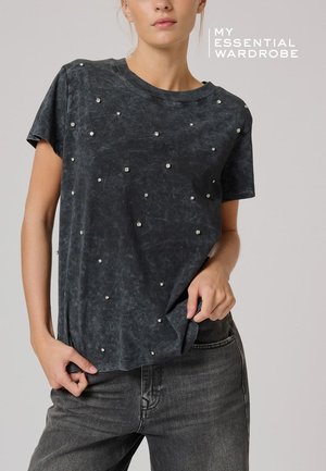 T-shirt gris foncé à manches courtes avec une texture usée et des clous métalliques éparpillés pour le détail. Coupe ajustée avec un col rond.