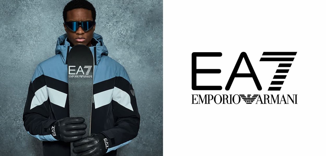 Chaqueta de invierno aislante en negro y azul con capucha, sosteniendo una tabla de snowboard negra con la marca EA7. Gafas de sol y guantes completan el conjunto.