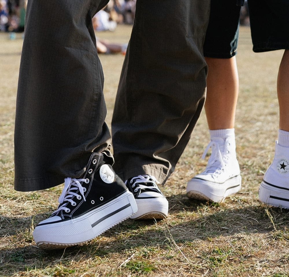 Black high-top sneakers with white soles and prominent rubber accents, paired with light-colored low-top sneakers on grass.