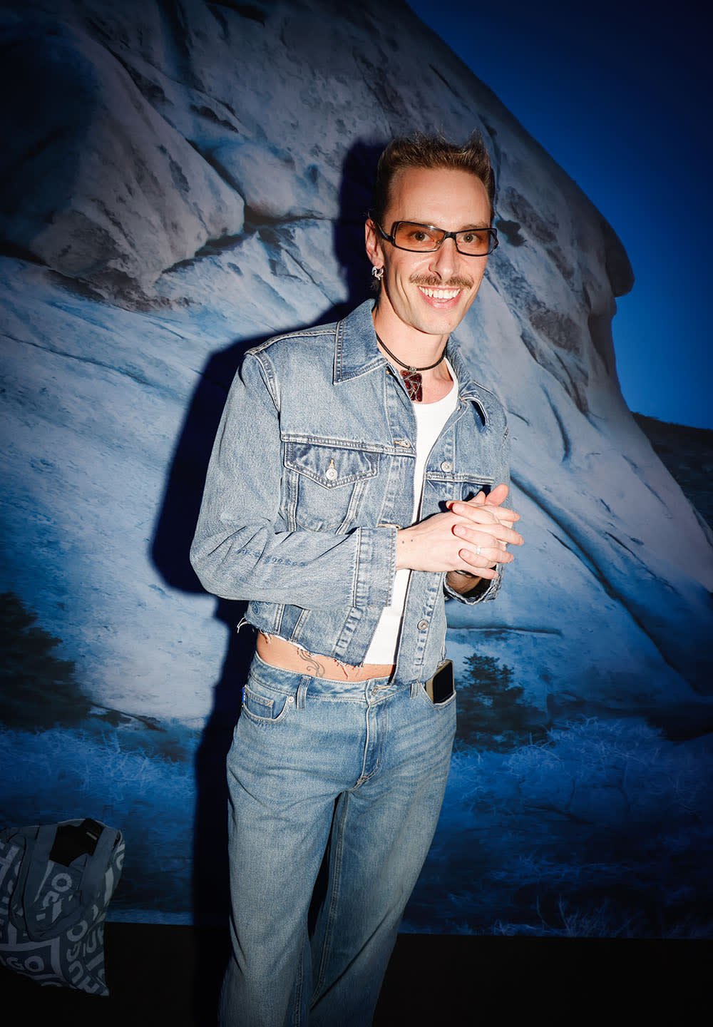 Denim jacket and jeans, both faded blue and cropped. White shirt underneath. Accessories include sunglasses, earrings, and a necklace.