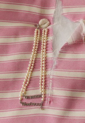 Tissu rayé rose et crème avec un bord effiloché, présentant un collier en perles avec une plaque nominative en argent "Vivienne Westwood".