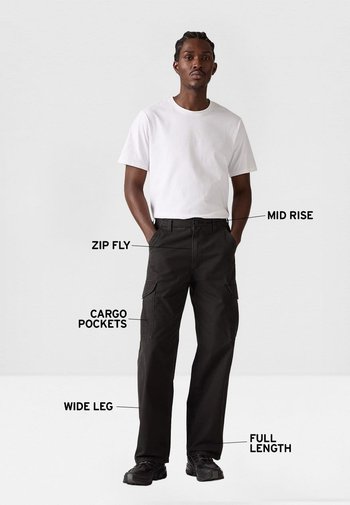 Pantalones cargo negros de pierna ancha, ajuste de talle medio, cremallera frontal y bolsillos cargo laterales; combinados con una camiseta blanca y zapatillas negras.