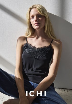 Schwarzes Camisole mit Spitzenbesatz, dünnen Trägern und kombiniert mit blauen Jeans. Glatte Textur mit lockerer Passform vor hellem Hintergrund.