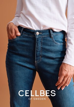 Dark blue denim jeans with a high waist, front pockets, and visible stitching details. Paired with a white long-sleeve shirt.