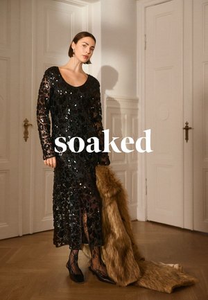 Abito lungo nero con paillettes e maniche lunghe, caratterizzato da una scollatura tonda e uno spacco laterale. Accompagnato da un coprispalle in pelliccia sintetica e calze velate in pizzo.