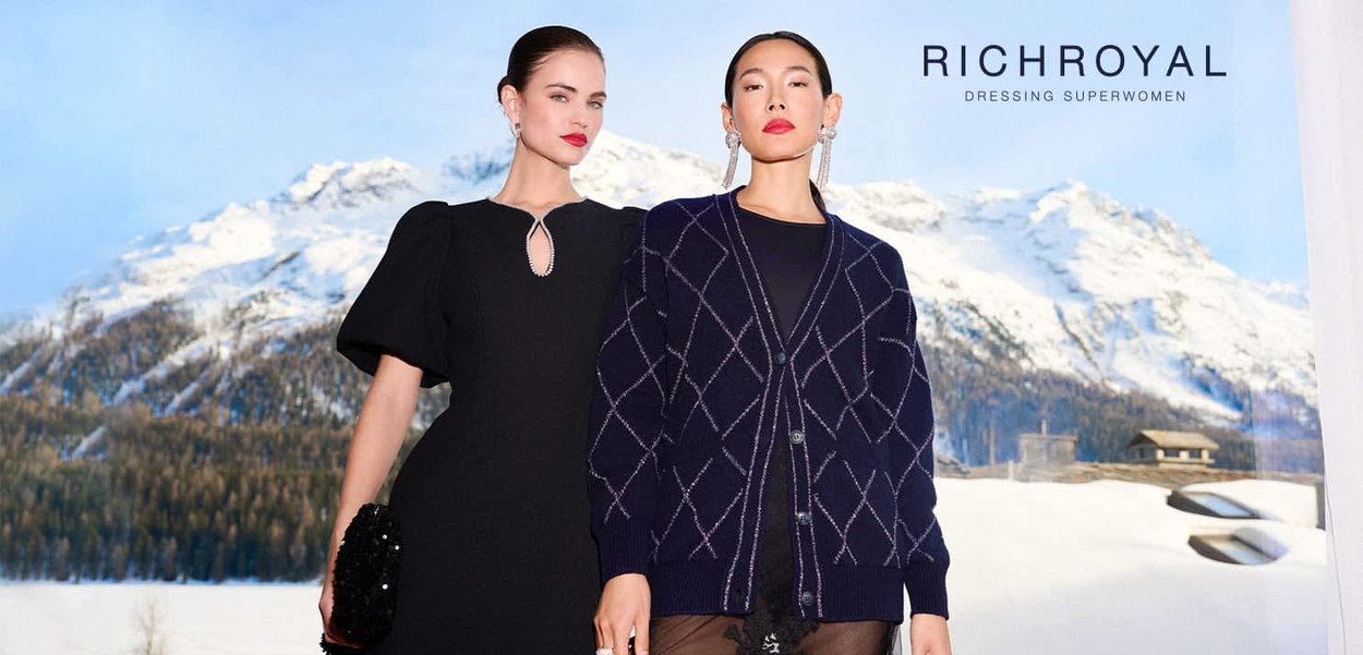 Schwarzes Kleid mit Puffärmeln und Schlitzdetail; marineblauer Cardigan mit Rautenmuster; schneebedeckte Berge im Hintergrund; Text "RICHROYAL DRESSING SUPERWOMEN."