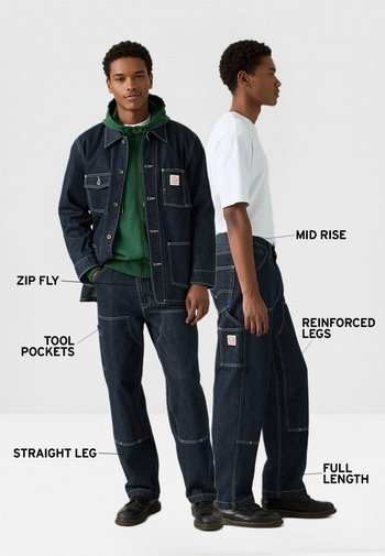 Chaqueta y pantalones de mezclilla oscura, con piernas rectas, ajuste de talle medio, cierre de cremallera, bolsillos para herramientas, piernas reforzadas, detalles con costuras y longitud completa.