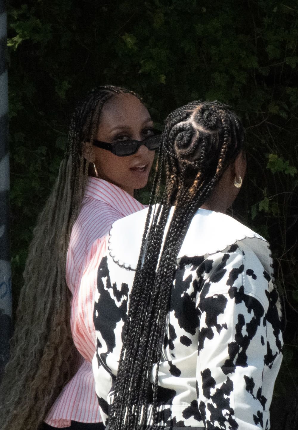 Twee personen met gevlochten haar dragen verschillende outfits: de één in een roze gestreept shirt en een zonnebril, de ander in een zwart-wit patroonjasje.