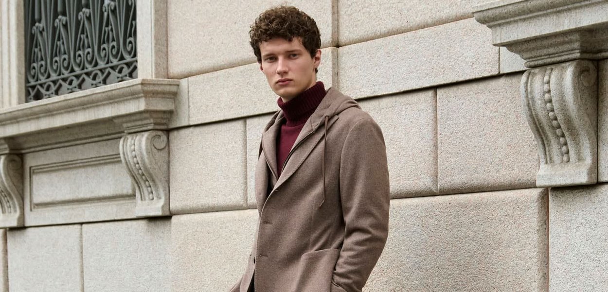 Bruine capuchonjas met een getailleerde pasvorm. Draagt over een bordeauxrode coltrui, met een gladde textuur en minimalistisch ontwerp.