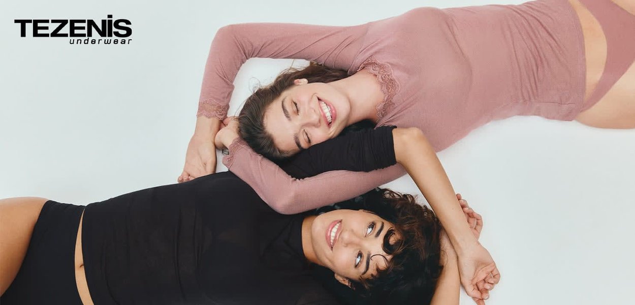 Two women lie side by side on a light background, wearing a pink lace-edged top and a black long-sleeve top, showcasing their relaxed poses.