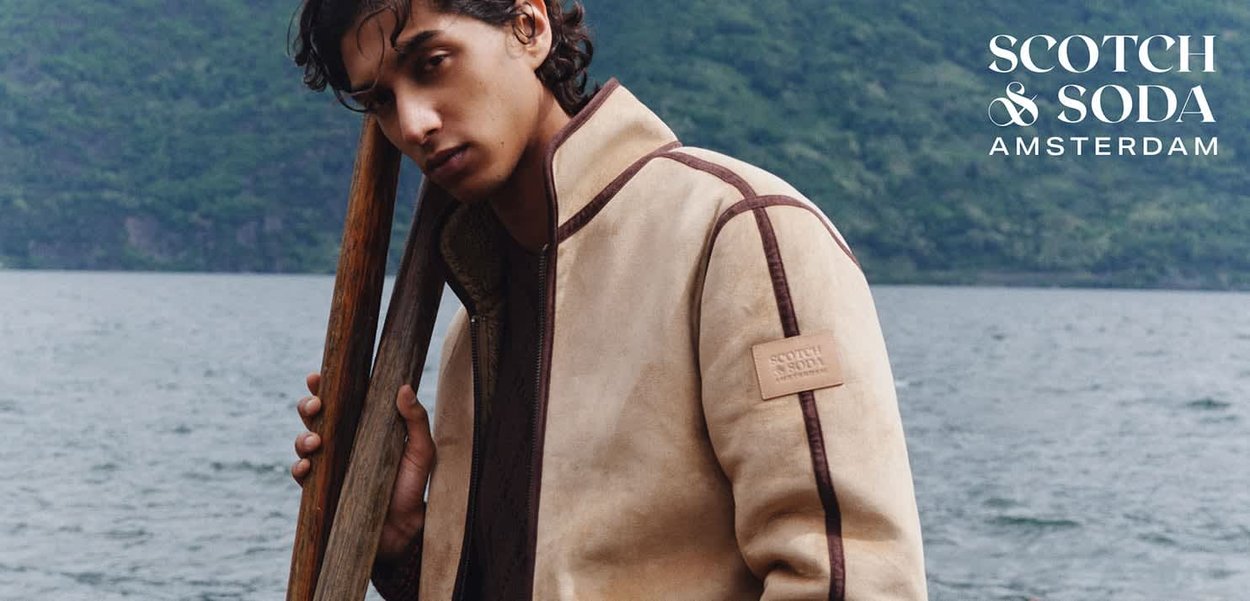 Veste bomber beige avec accents et doublure marron, dotée d'un col montant et d'un tissu texturé. Patch logo de la marque sur la manche gauche.