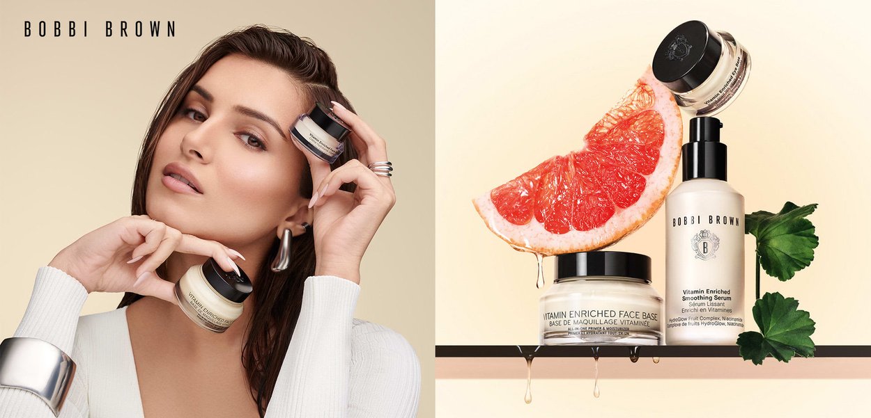 Bobbi Brown Vitamin Enriched Face Base in a clear jar, cream texture, with a black lid; a grapefruit slice drips above it on a light background.