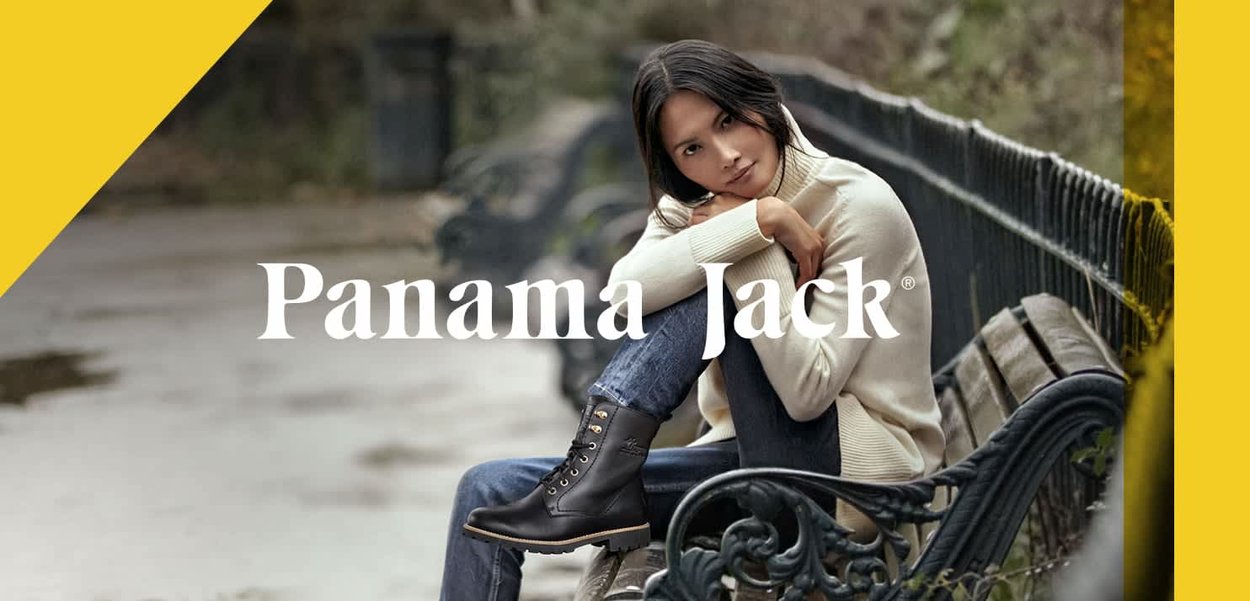 Black leather ankle boots with laces and a sturdy sole. The model wears a cream sweater and blue jeans, sitting on a park bench.