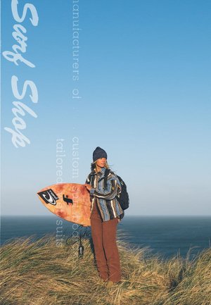 Een persoon in een gestreepte, multikleuren jas en bruine broek staat op gras, met een oranje surfplank in zijn handen. Op de achtergrond is er een blauwe lucht en zee.