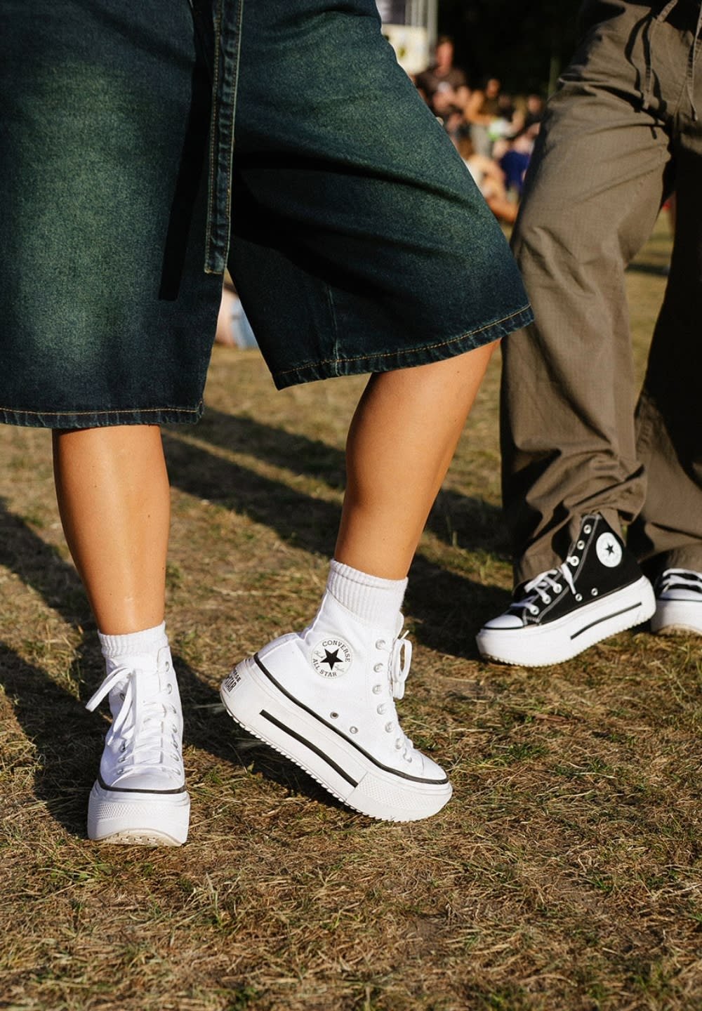 White platform high-top sneakers with black stripes, white eyelets, and a circular logo. Worn with white ankle socks and dark denim shorts.