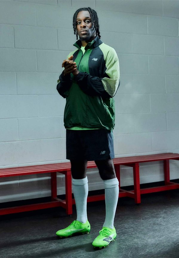 Tenue de sport comprenant une veste verte et noire, un short noir, des chaussettes blanches et des crampons de foot vert fluo. Accent sur le design fonctionnel des vêtements de sport.