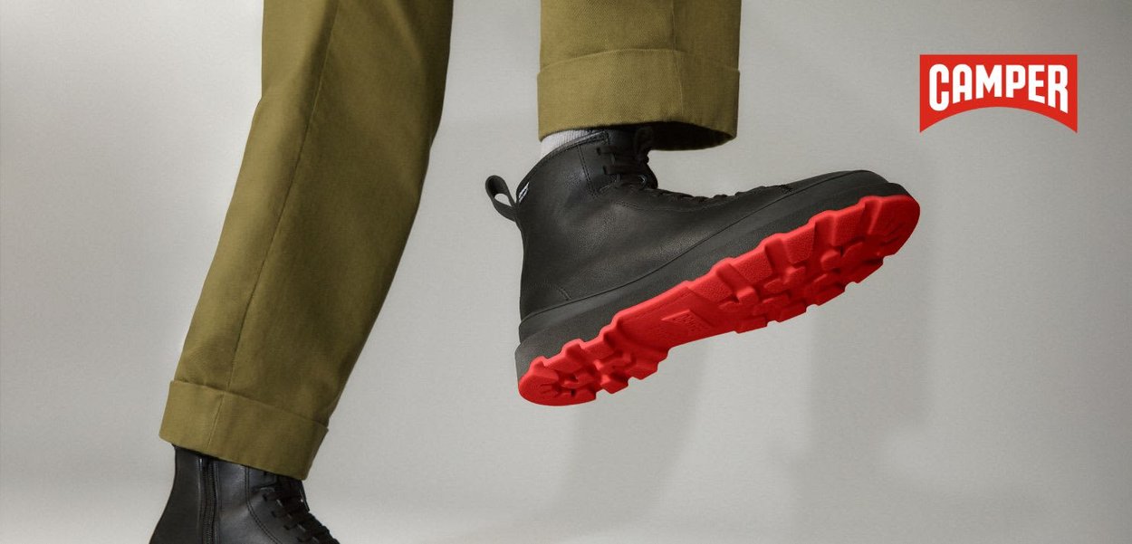 Schwarzer Schnürstiefel aus strukturiertem Leder mit roter Gummisohle und hohem Schaft, kombiniert mit olivgrünen, zulaufenden Hosen.