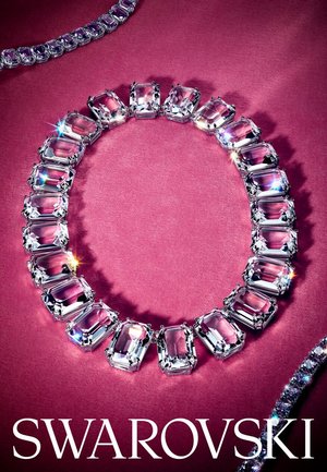 Collier en cristal mettant en avant des pierres rectangulaires transparentes serties dans du métal, affichant un éclat brillant sur un fond rose texturé.